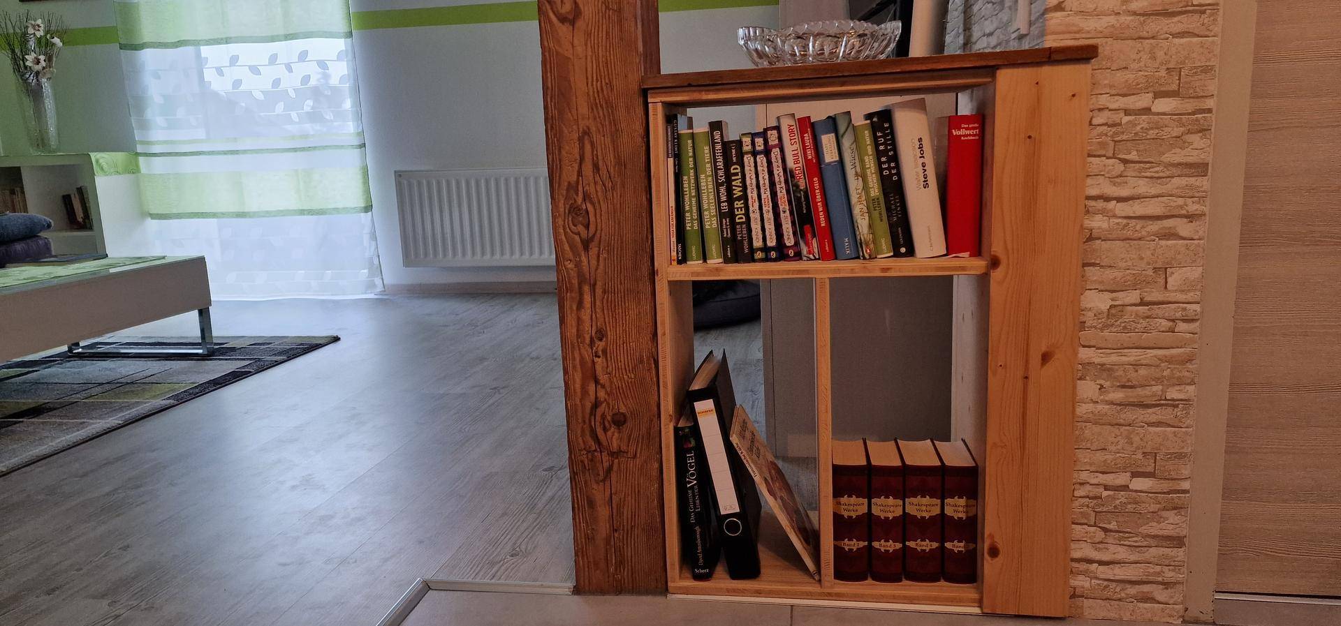 Rustikales Holzregal mit Büchern, integriert in den Wohnbereich mit Laminatboden und hellem Fenster.