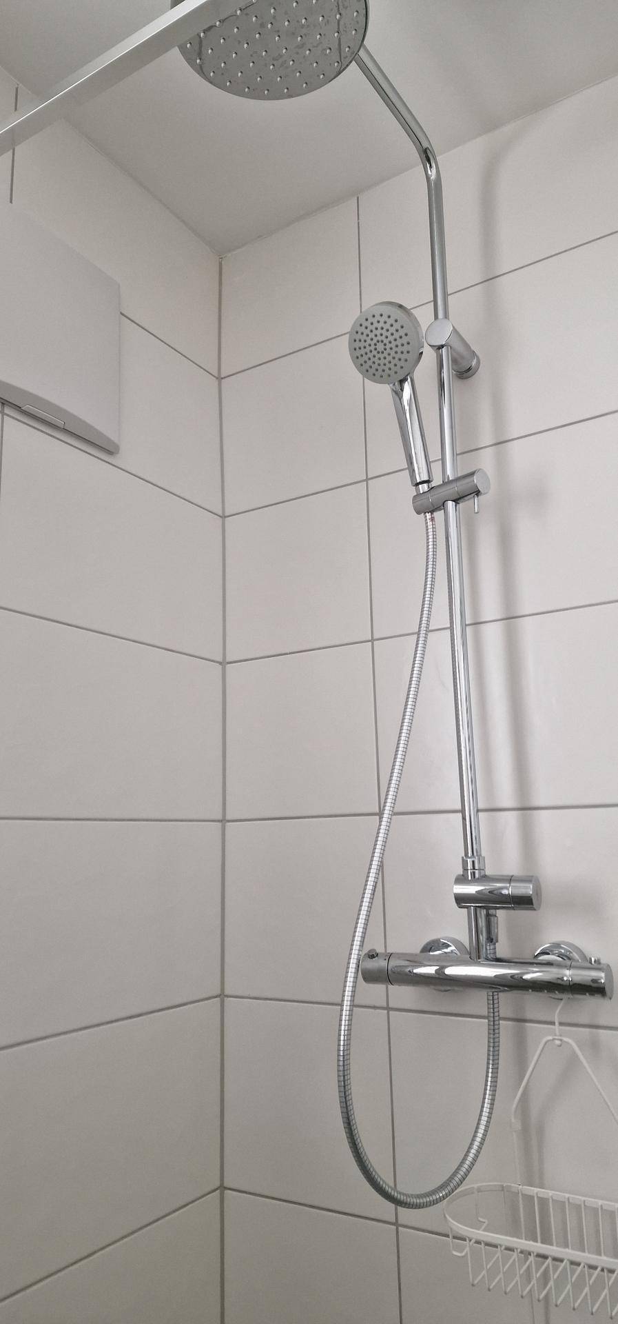 Duschkopf und Handbrause in einem modernen Badezimmer mit weißen Fliesen.