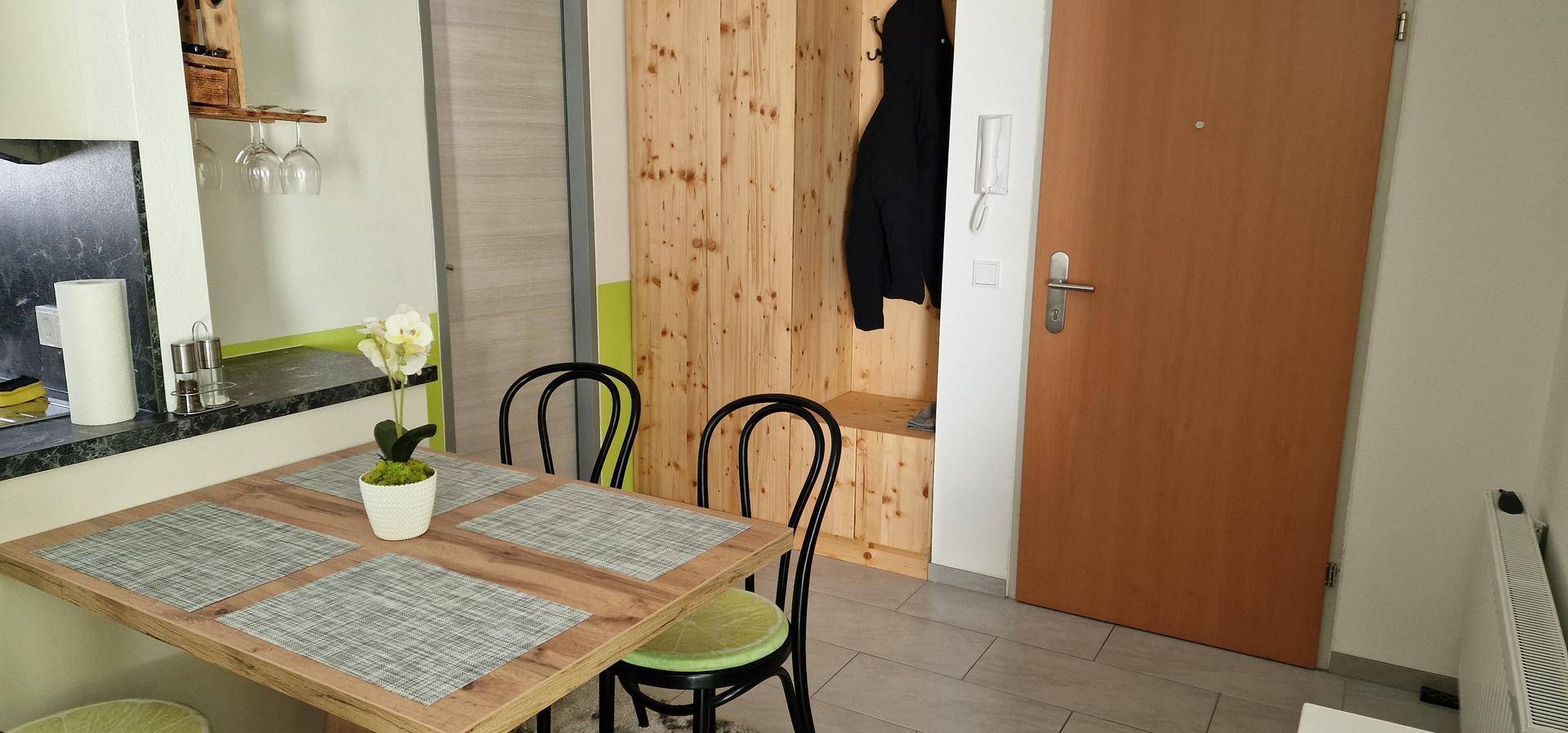 Eingangsbereich mit Esstisch, Holzschrank und einer braunen Tür, die zum Wohnbereich führt.