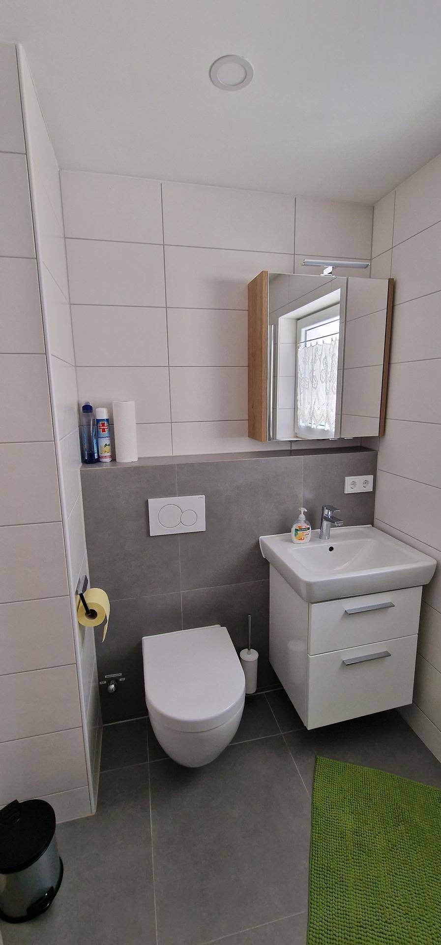 Helles Badezimmer mit Wand-WC, Waschbecken und Spiegelschrank, in modernen Grautönen gestaltet.