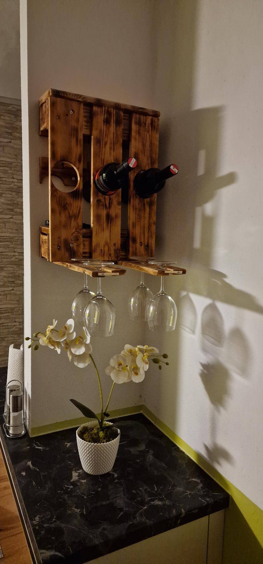 Dekoratives Weinregal aus Holz mit Flaschen und hängenden Gläsern über einer Orchideenpflanze.