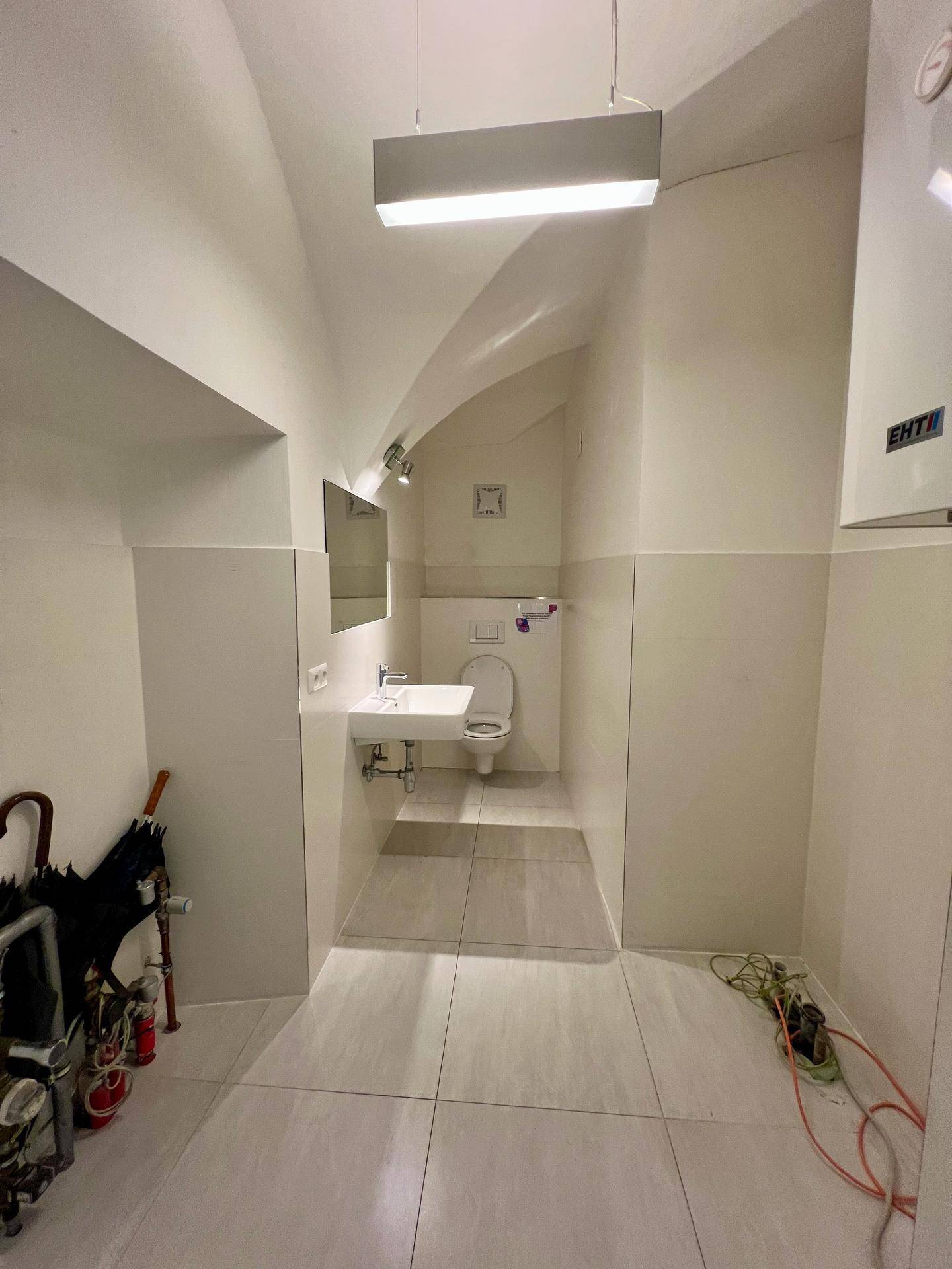 Badezimmerbereich mit Waschbecken, Toilette und einem Heizkessel an der Wand, unter Gewölbedecken.