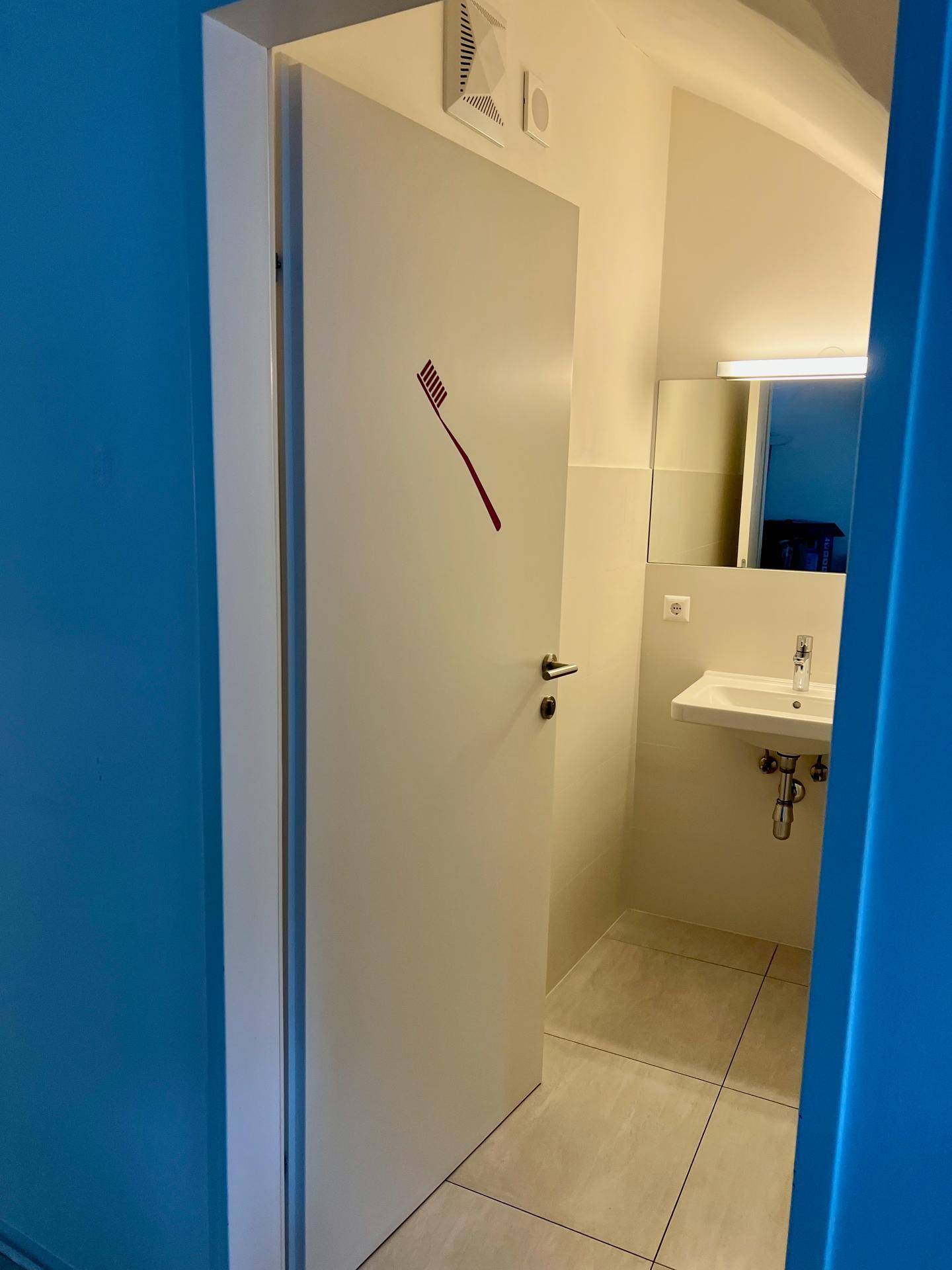 Eingang zu einem Badezimmer mit einer weißen Tür, die mit einem Zahnbürstensymbol versehen ist.