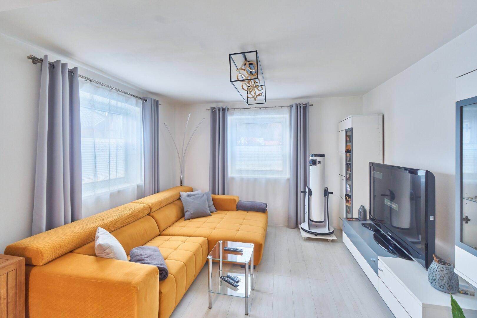 Gemütliches Wohnzimmer mit einem großen gelben Ecksofa, Couchtisch und Fernseher für entspannte Abende.