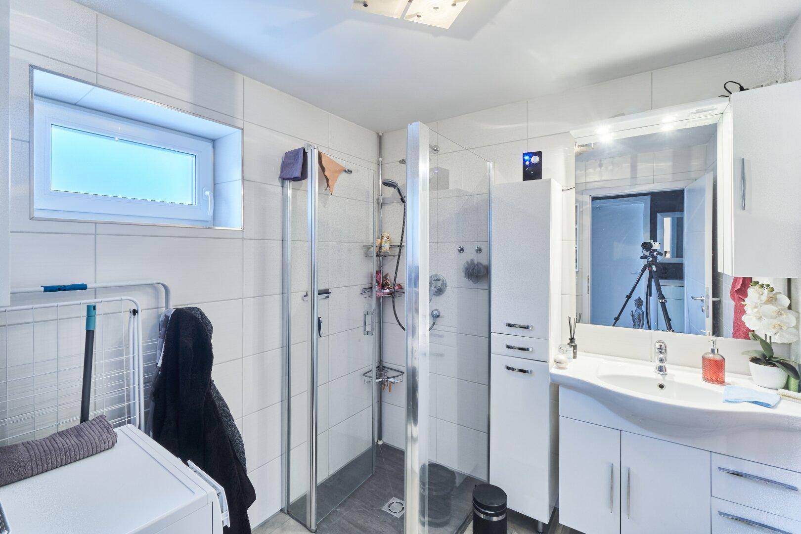 Modernes Badezimmer mit ebenerdiger Dusche, Waschbecken, Spiegelschrank und einem Fenster für Belüftung.