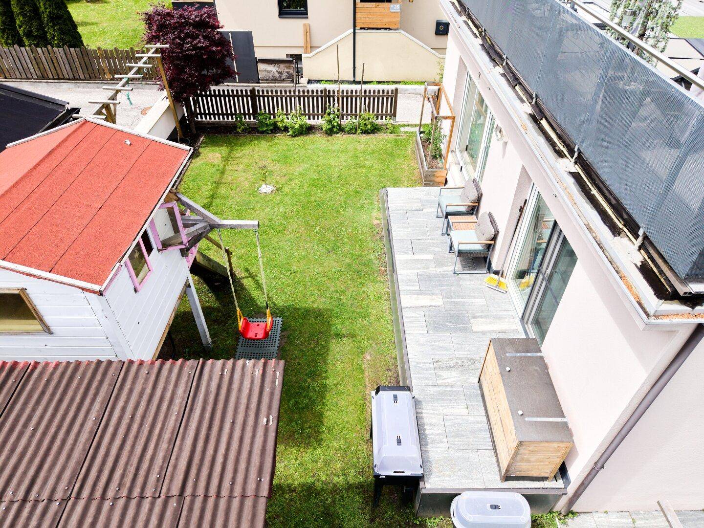 Gepflegter Gartenbereich mit Rasenfläche, Terrasse, Kinderspielhaus und einem Grillplatz für Familien.