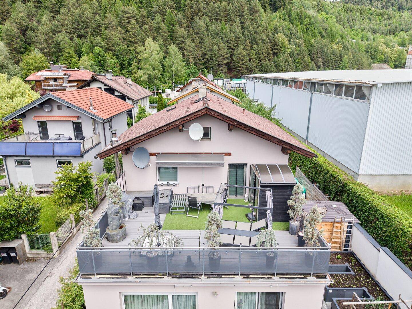 Große Dachterrasse mit Kunstrasen, Gartenmöbeln und einem weiten Blick auf die bewaldeten Hügel.