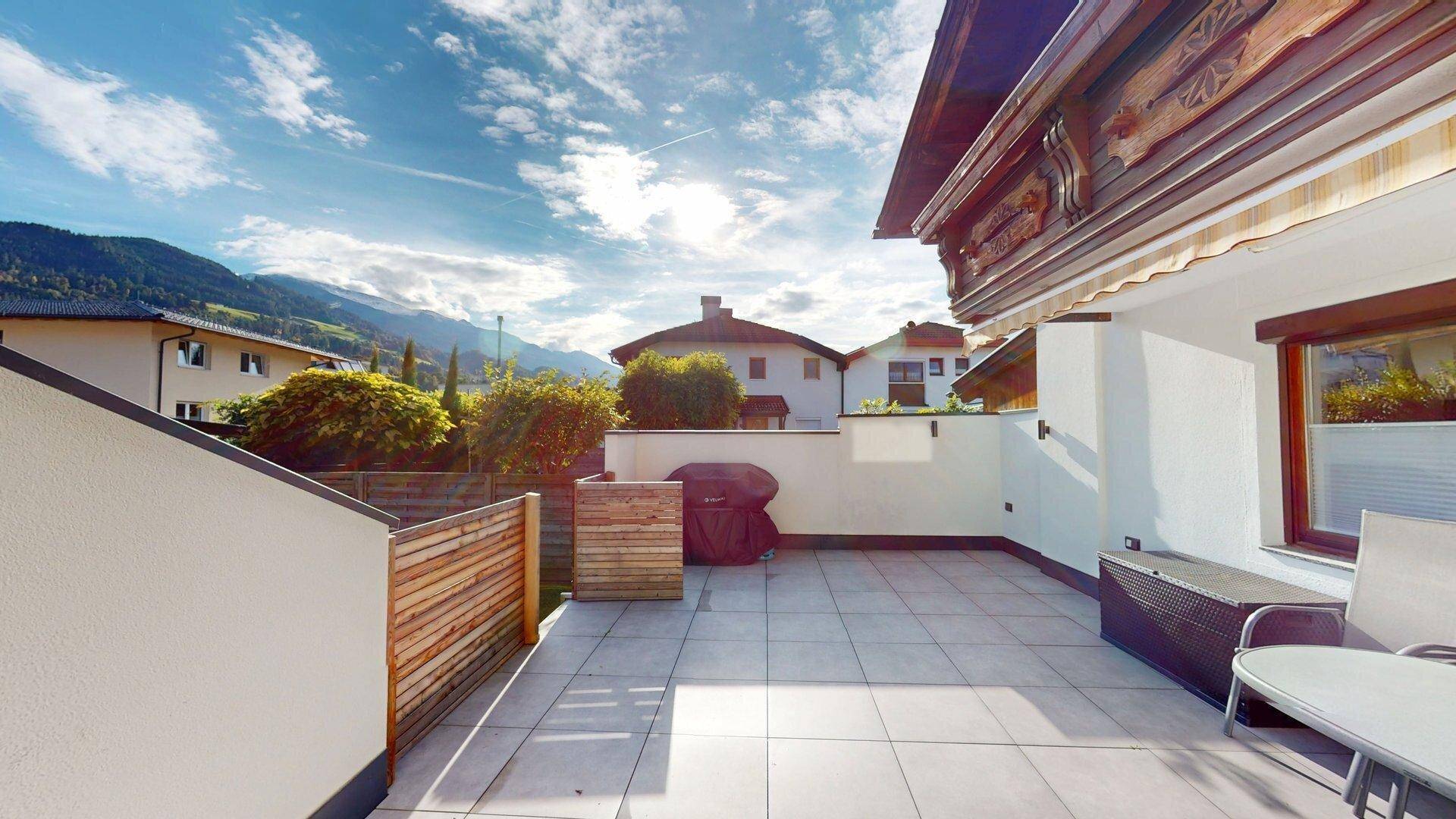 Geräumige Terrasse mit Fliesenboden, Grillbereich und einem malerischen Bergblick unter blauem Himmel.