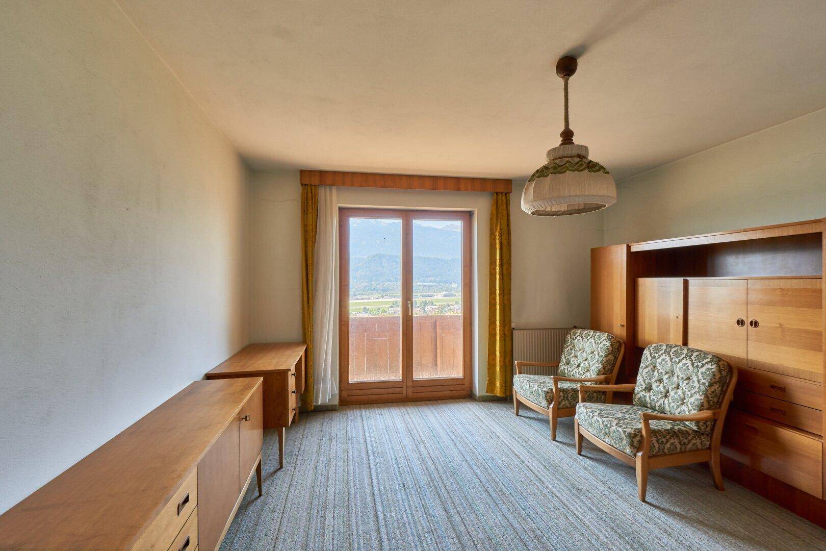 Schlafzimmer mit Teppichboden, Holzmöbeln und Zugang zu einem Balkon mit Bergblick.