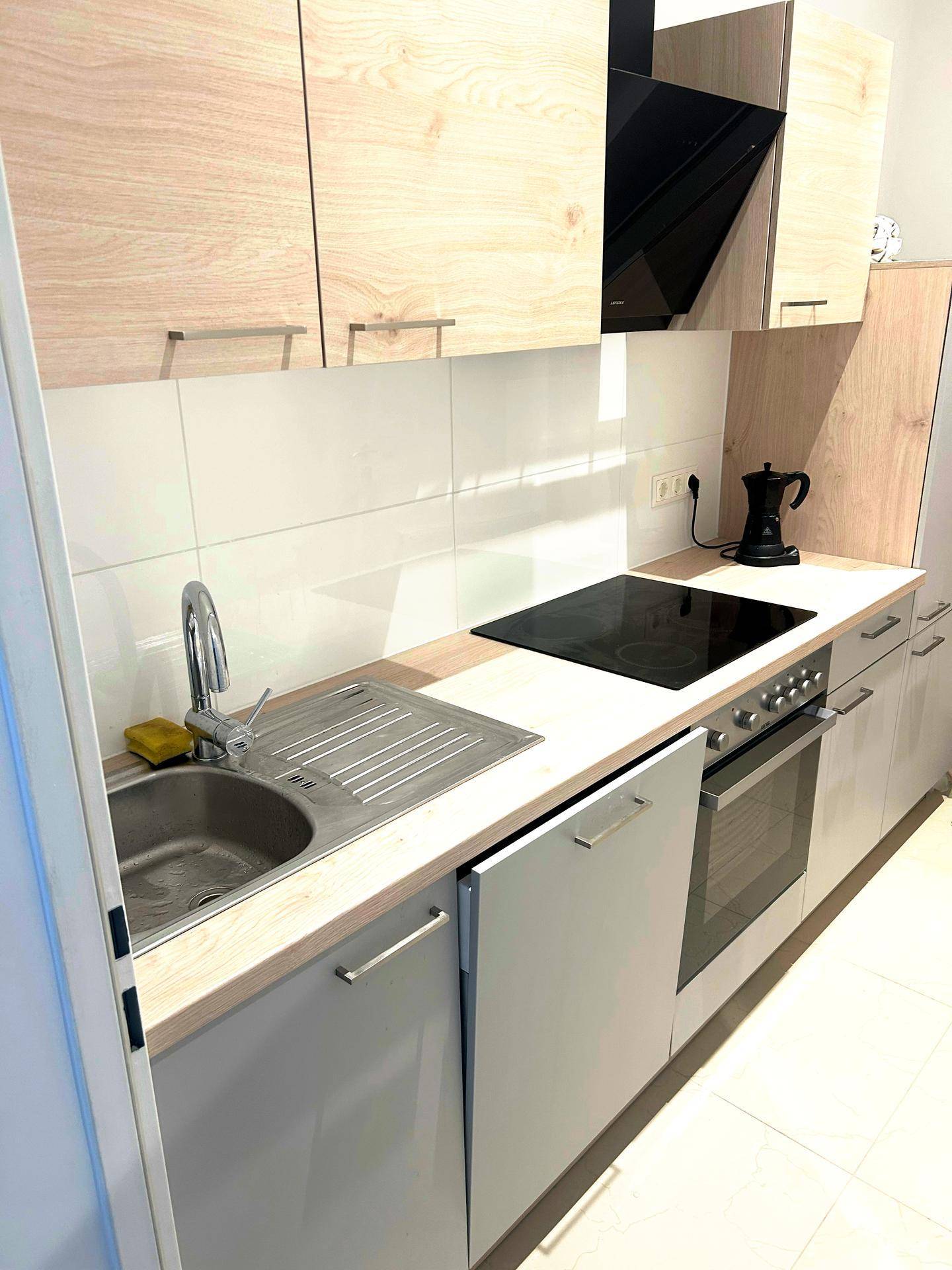 Moderne Küche mit hellen Holzfronten, Induktionskochfeld, Backofen und integriertem Geschirrspüler.
