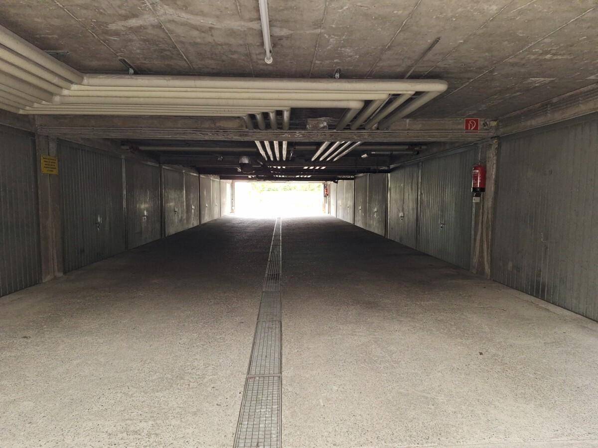 Langer Gang einer Tiefgarage mit Reihen von Garagenboxen und sichtbaren Leitungen an der Decke.