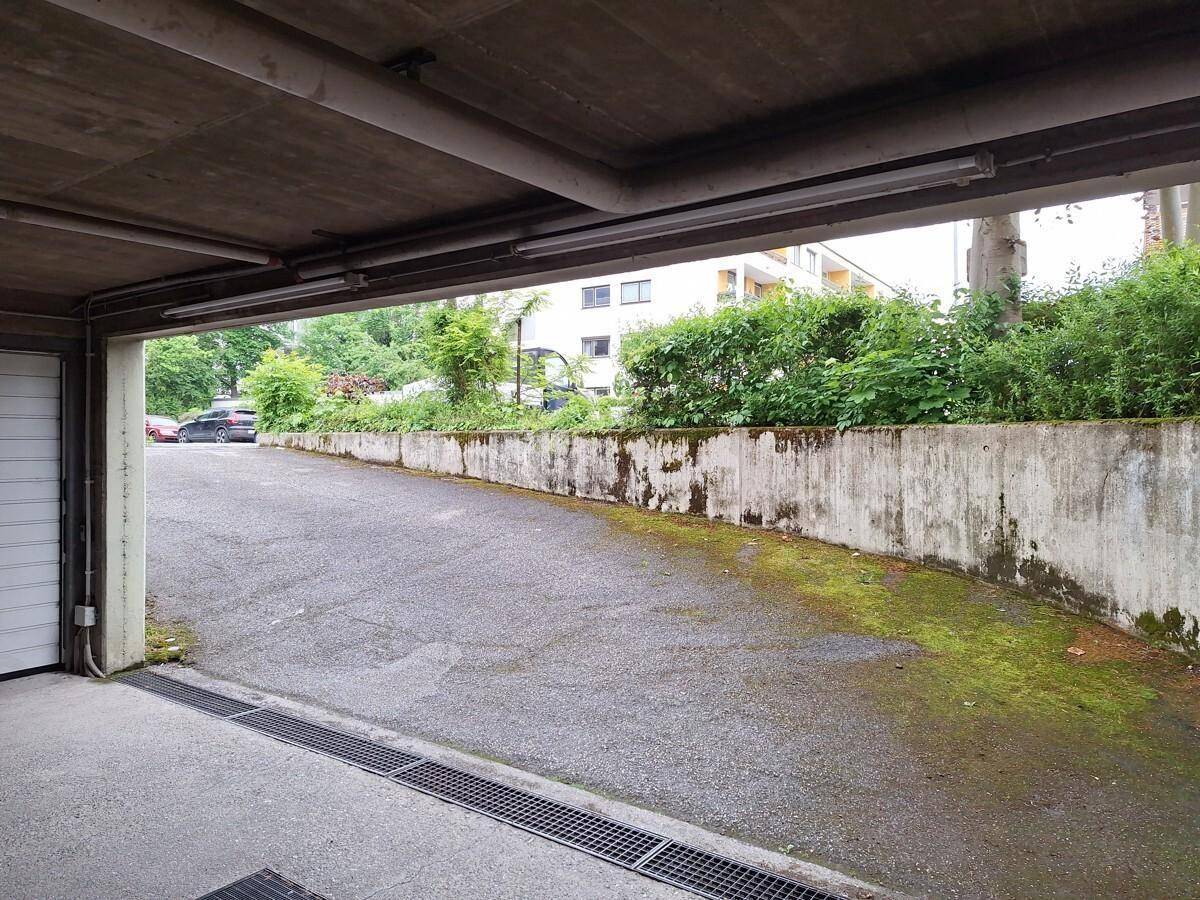 Ausfahrt einer Tiefgarage mit Blick auf eine begrünte Außenanlage und ein Wohngebäude.