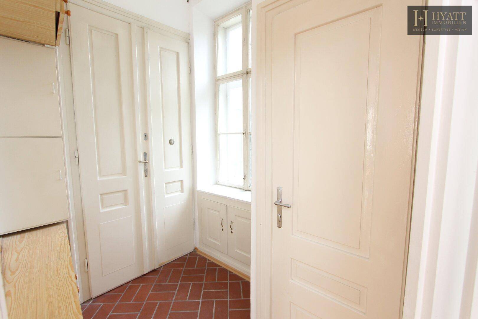 Eingangsbereich der Wohnung mit Terrakotta-Fliesen und mehreren Türen.
