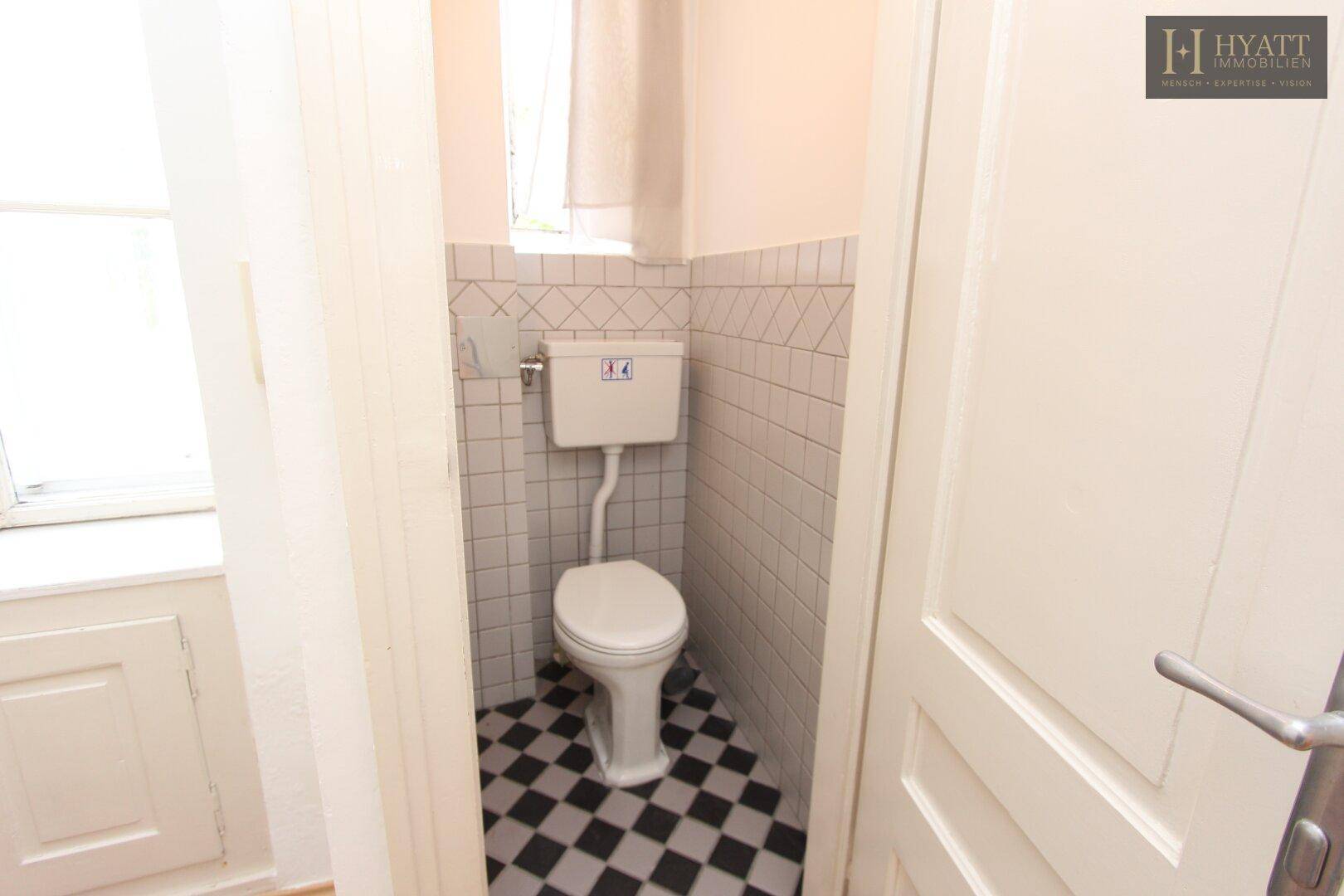 Kleines Gäste-WC mit schwarz-weiß karierten Fliesen und Fenster.