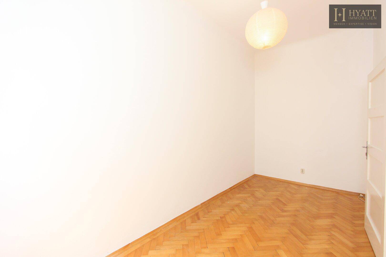 Ruhiges Zimmer mit hellem Fischgrätparkett und einfacher Deckenleuchte.