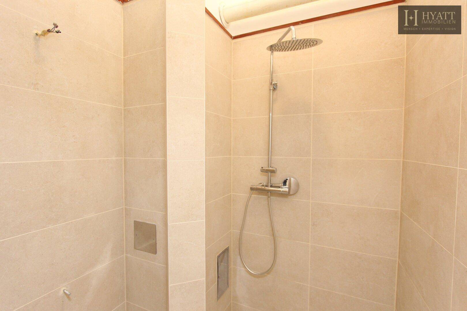 Geräumige Dusche mit beigefarbenen Fliesen und moderner Regendusche.