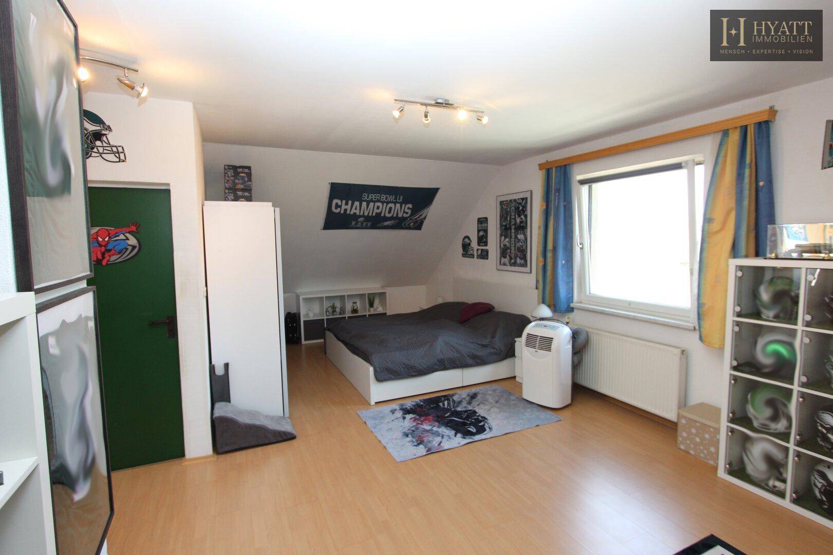 Gemütliches Schlafzimmer im Dachgeschoss mit Holzboden, Bett und Schräge.