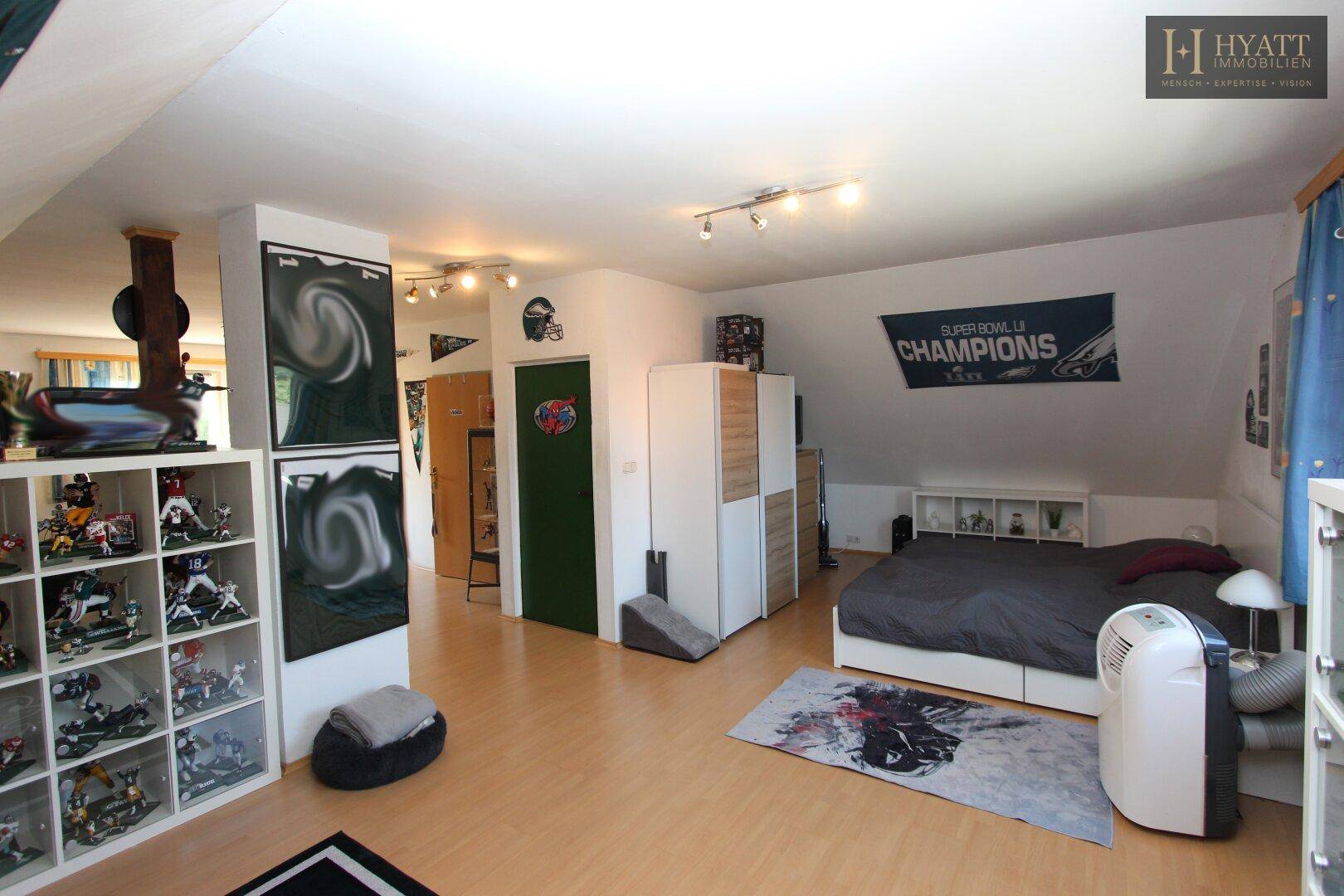 Großes Schlafzimmer im Dachgeschoss mit Holzboden, Bett und Blick auf den angrenzenden Bereich.