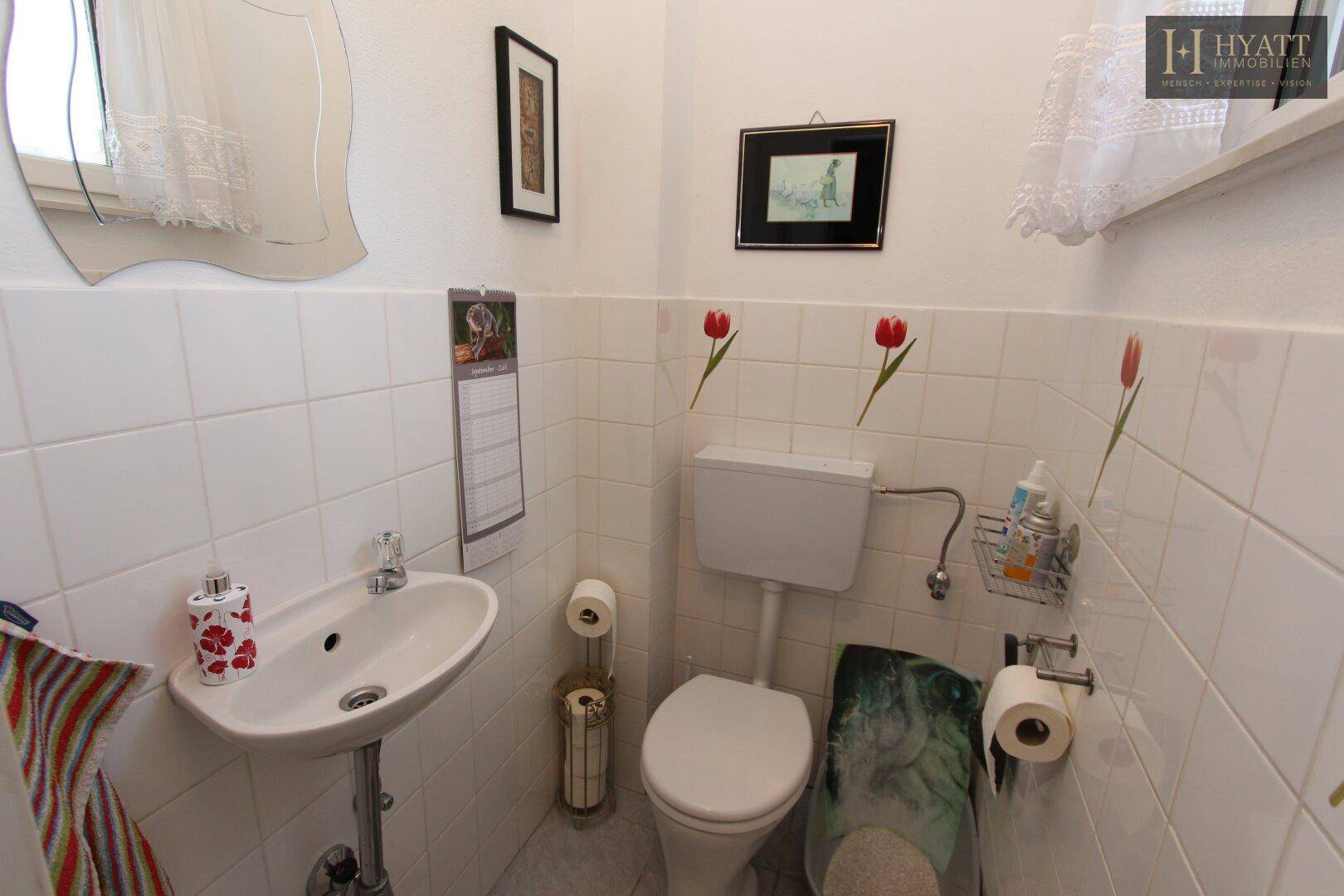 Kleines Gäste-WC mit weißen Fliesen, Waschbecken und Fenster für Tageslicht.
