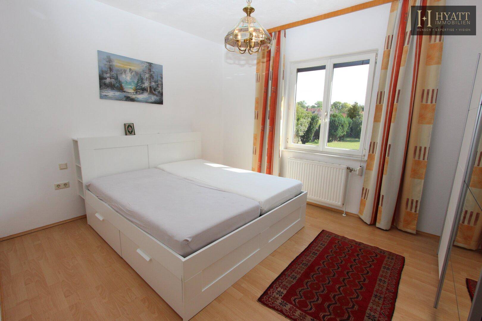 Helles Schlafzimmer mit Holzboden, Doppelbett und Fenster mit Blick ins Grüne.