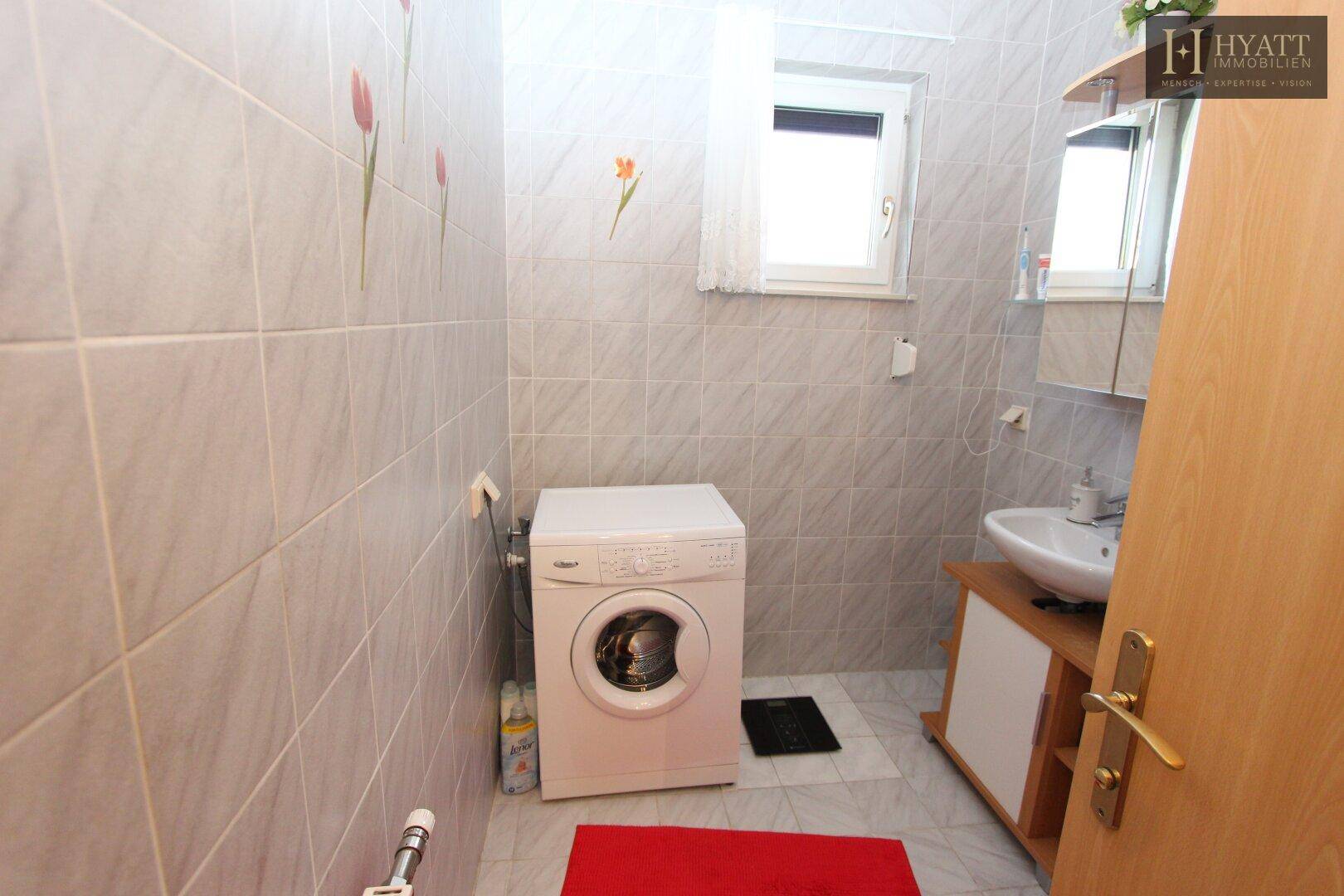Badezimmer mit Waschmaschine, Waschbecken und Fenster, praktisch als Hauswirtschaftsraum.