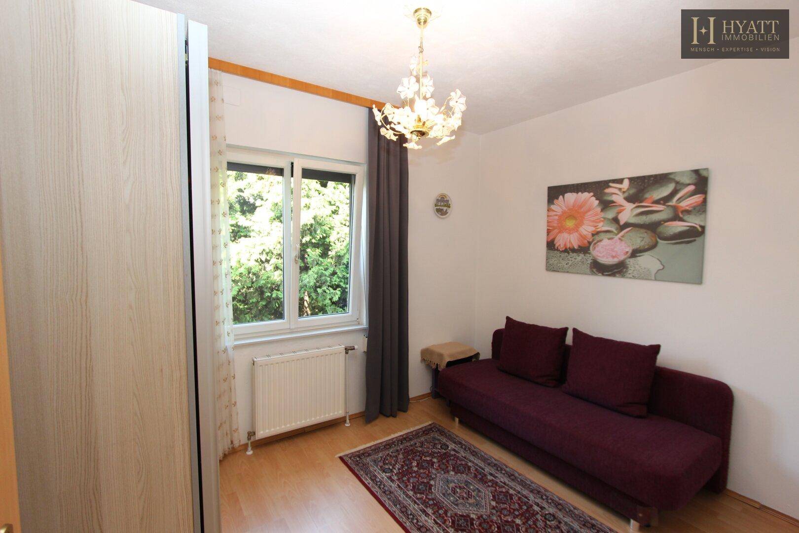 Freundliches Zimmer mit Holzboden, Schlafsofa und Fenster mit Blick in den Garten.