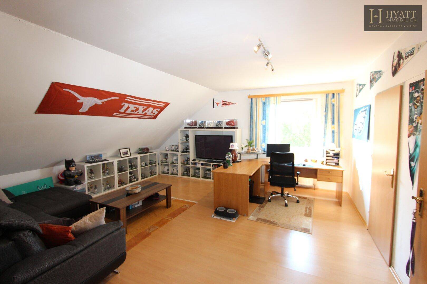 Geräumiges Dachgeschosszimmer mit Schreibtisch, Sofa und viel Stauraum unter der Dachschräge.