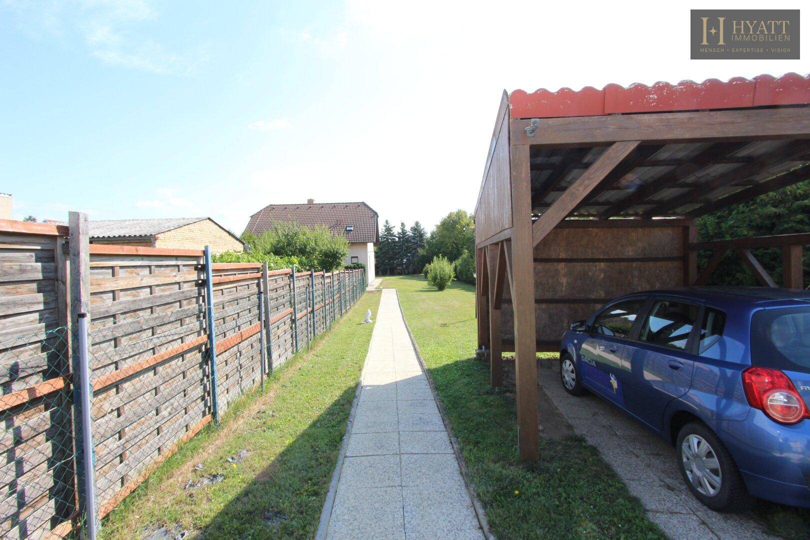 Langer Gartenweg führt zu einem Carport mit einem geparkten blauen Auto.