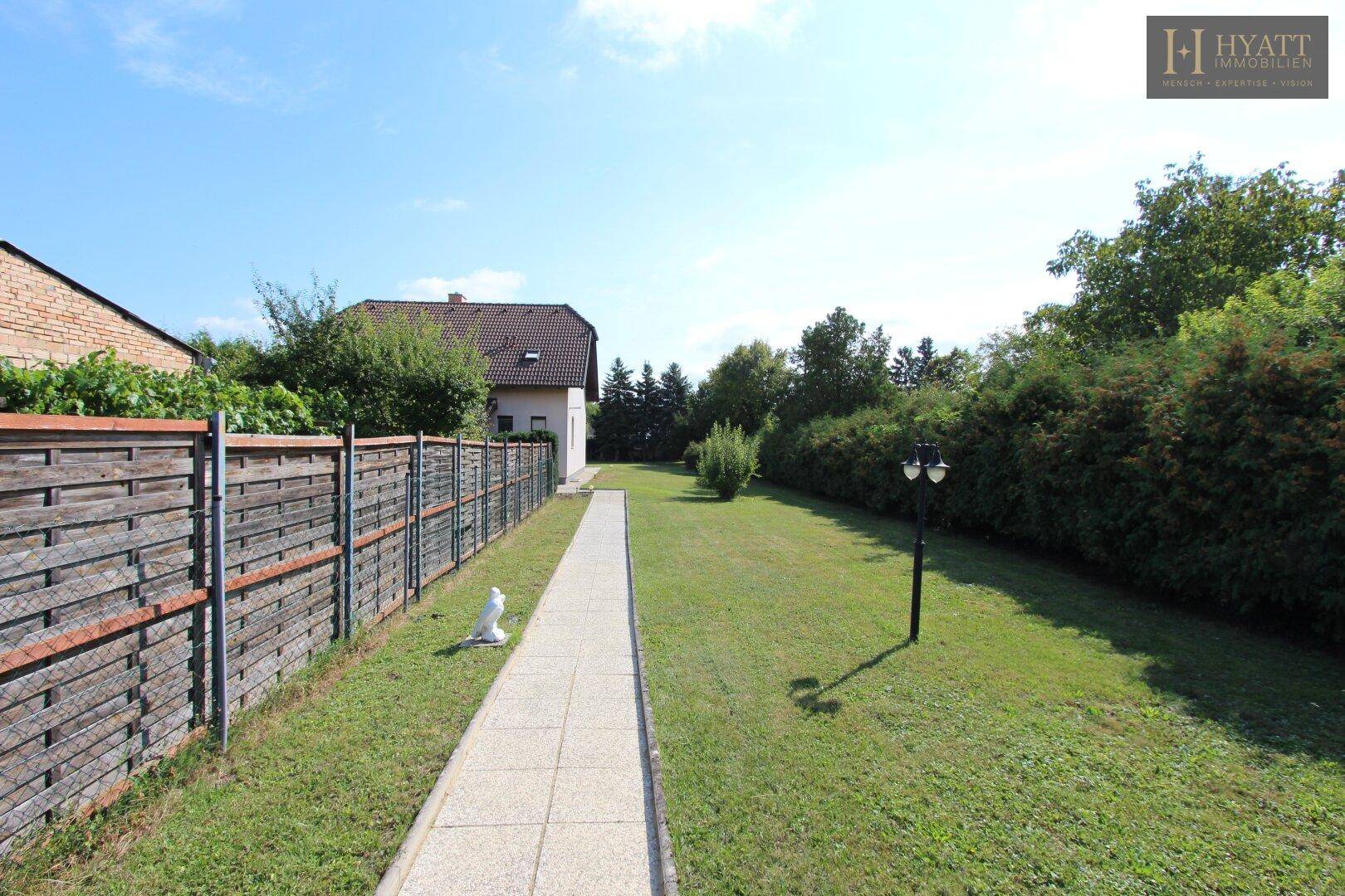 Langer Gartenweg führt durch eine gepflegte Rasenfläche zu einem Einfamilienhaus.