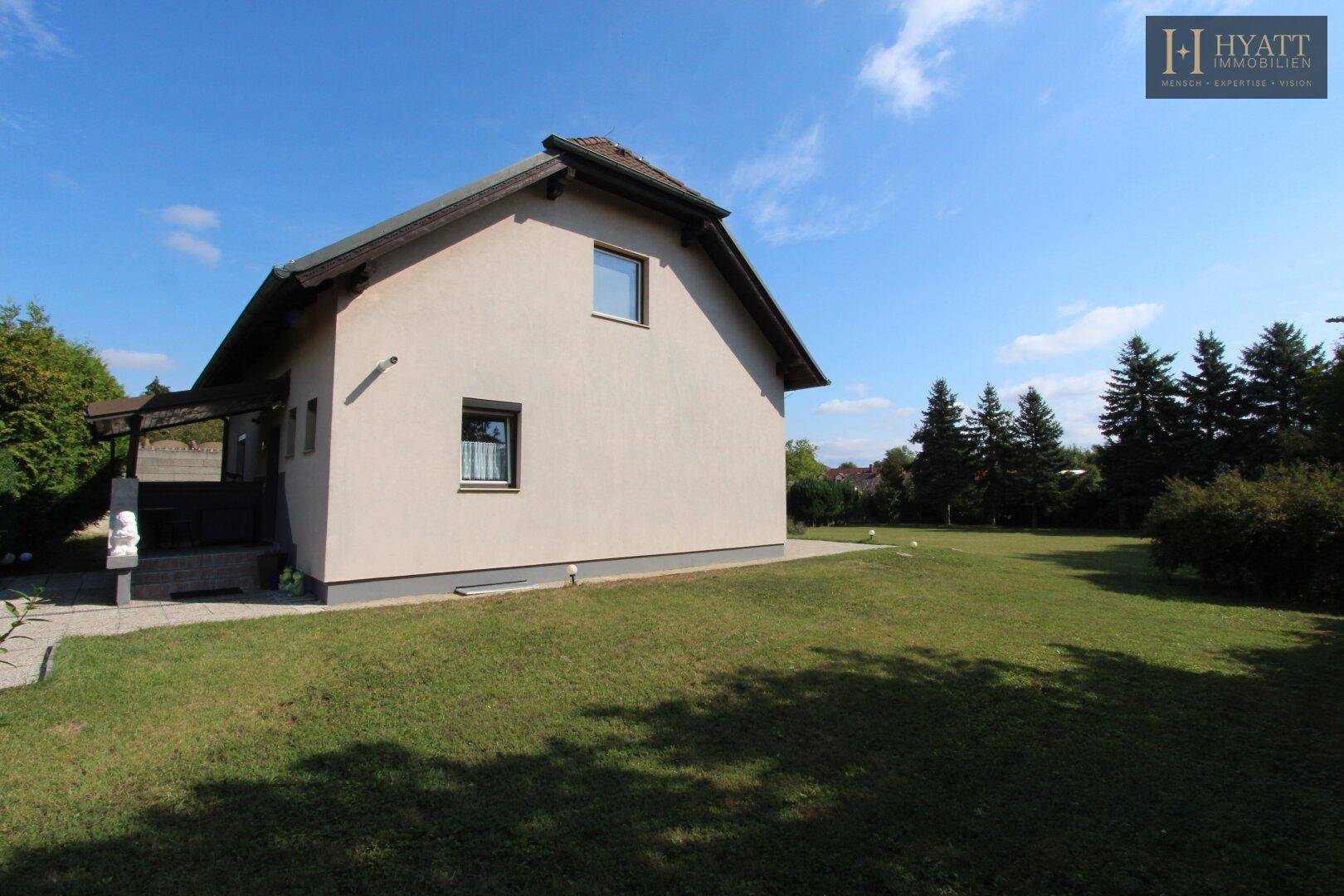 Seitenansicht eines Einfamilienhauses mit großem, sonnigen Garten und hohen Bäumen.