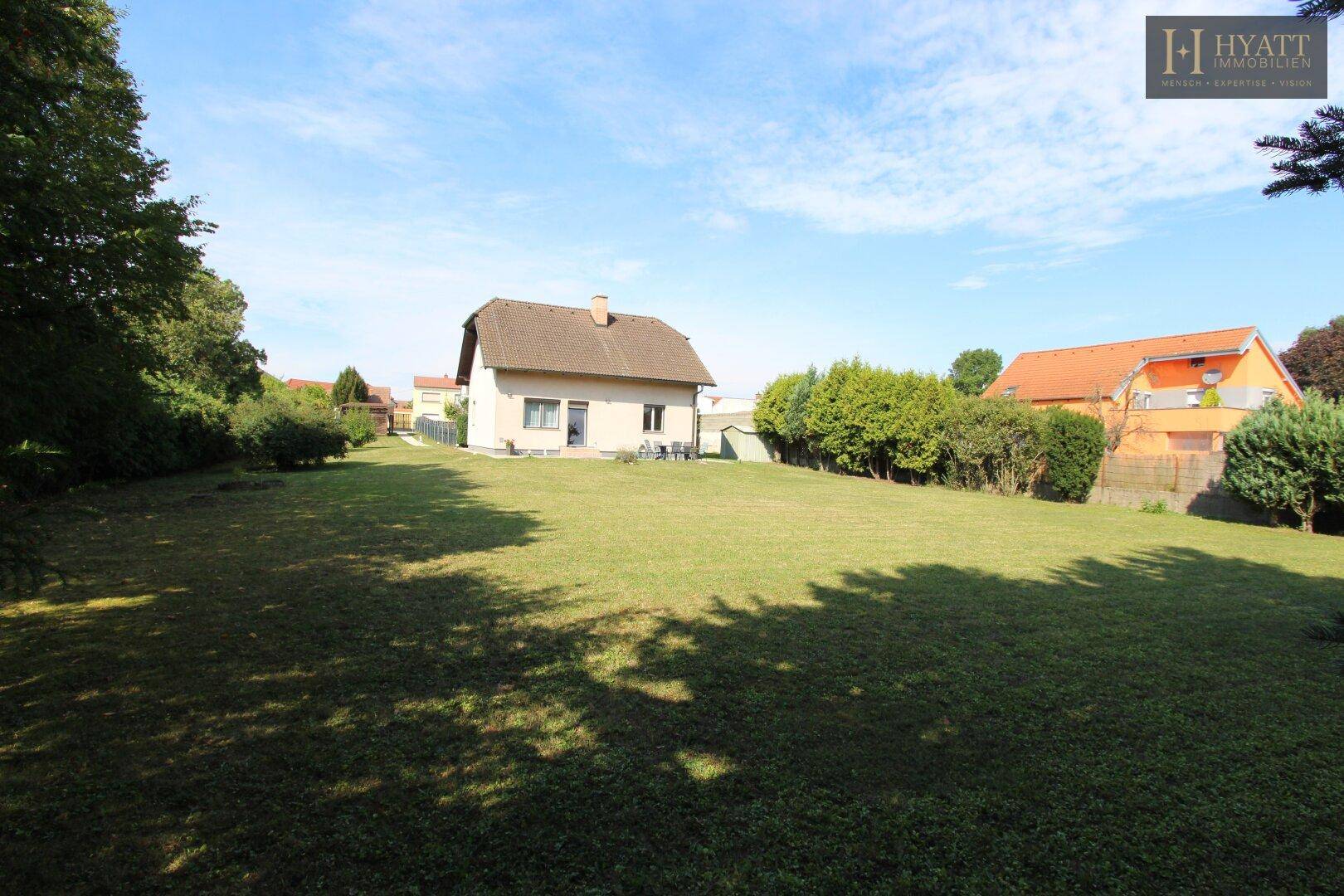 Weitläufiger Garten mit großer Rasenfläche und dem Einfamilienhaus im Hintergrund an einem sonnigen Tag.