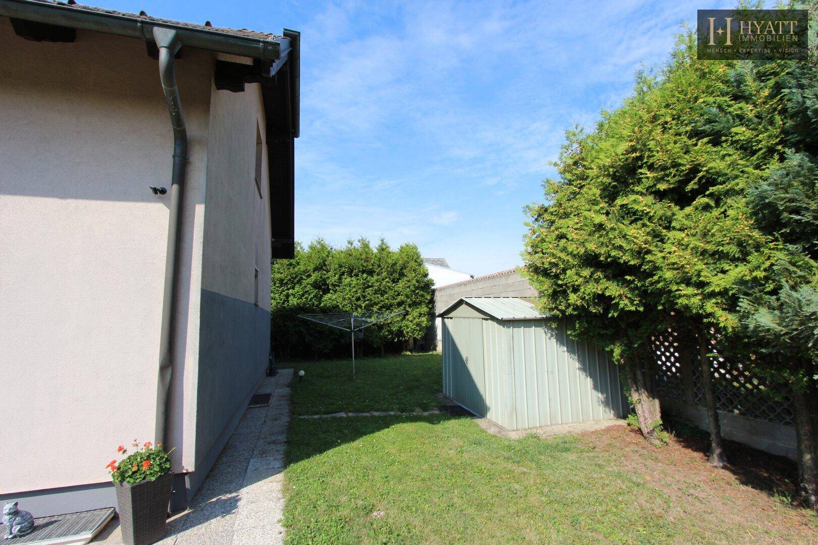 Seitlicher Gartenbereich mit Gartenhaus, gepflegter Hecke und Zugang zum Haus.