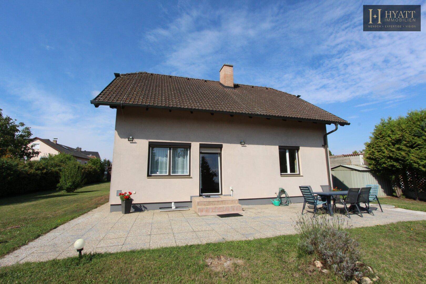 Rückseite des Hauses mit großer Terrasse, Gartenmöbeln und Zugang zum weitläufigen Garten.