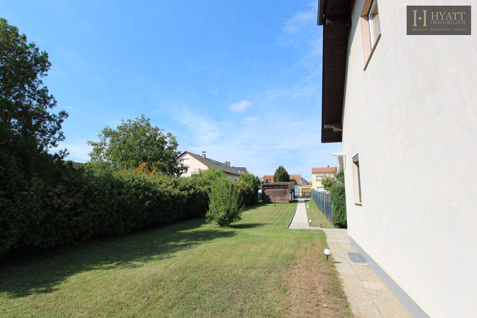 Seitenansicht des Hauses mit gepflegtem Rasen und einer hohen Hecke, die Privatsphäre bietet.