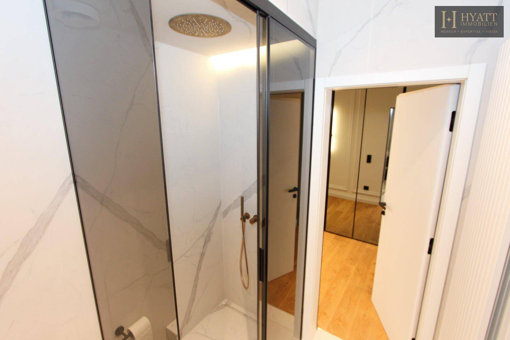 Elegantes Badezimmer mit großer begehbarer Dusche und Marmorfliesen an den Wänden.