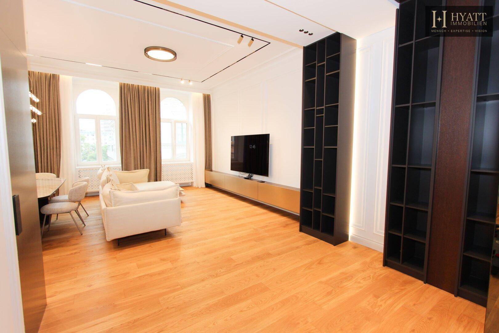 Geräumiger Wohnbereich mit Holzboden, integrierten Regalen und großem Fernseher.