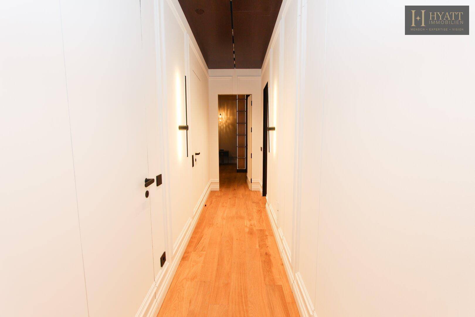 Langer, heller Flur mit Holzboden und eleganten Wandleuchten.