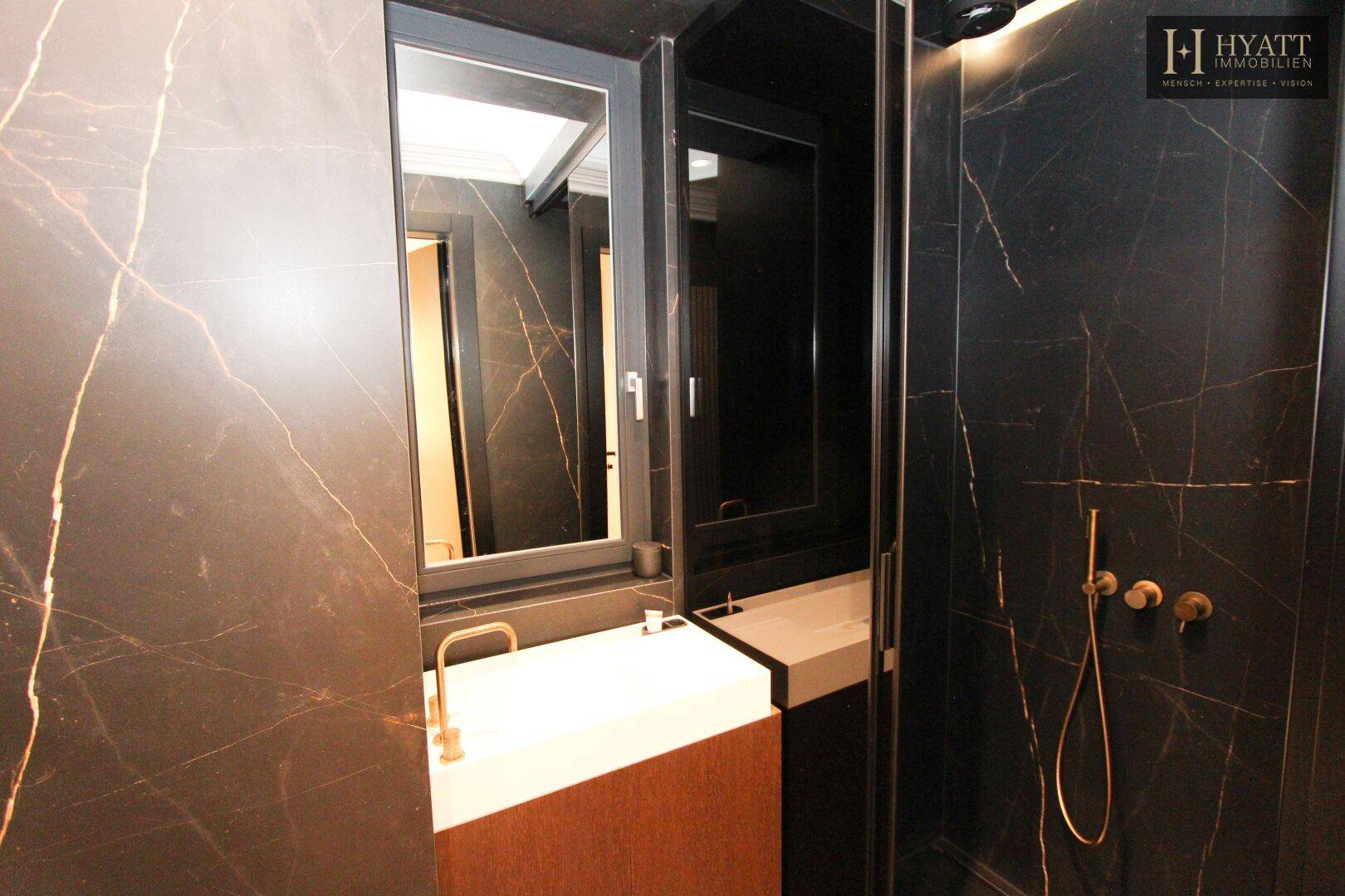 Dunkles, luxuriöses Badezimmer mit Marmorfliesen, modernem Waschbecken und Dusche.