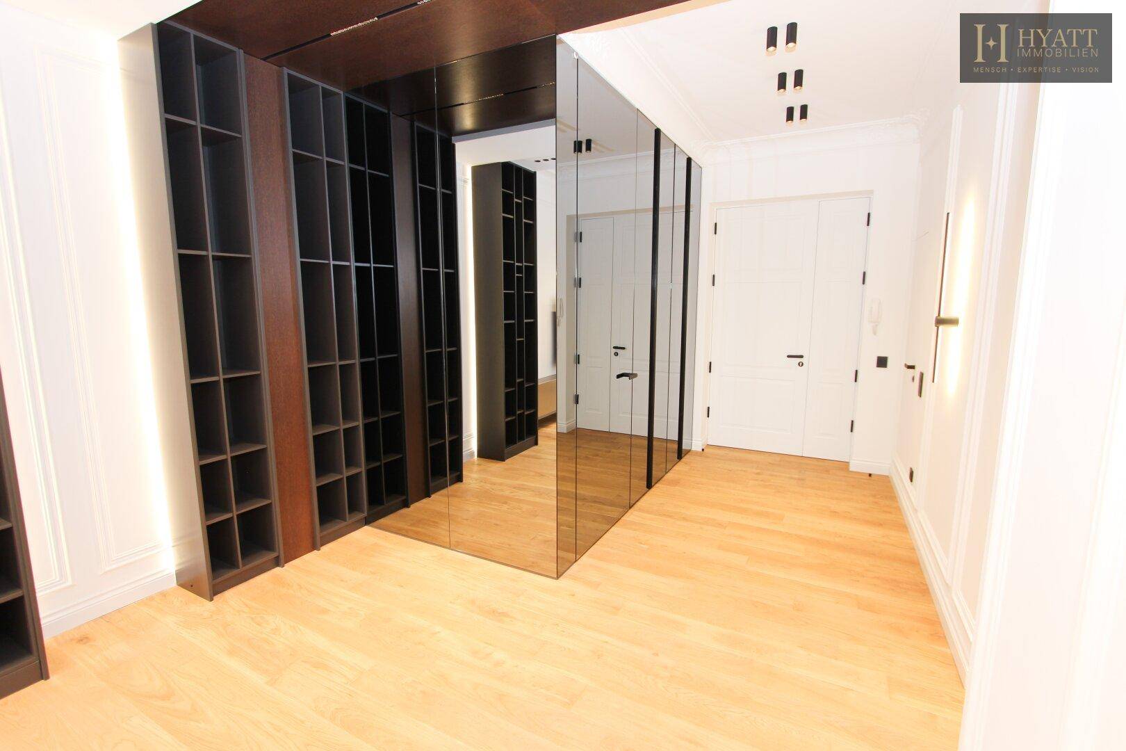 Heller Flur mit Holzboden, Spiegelflächen und integrierten dunklen Regalen.