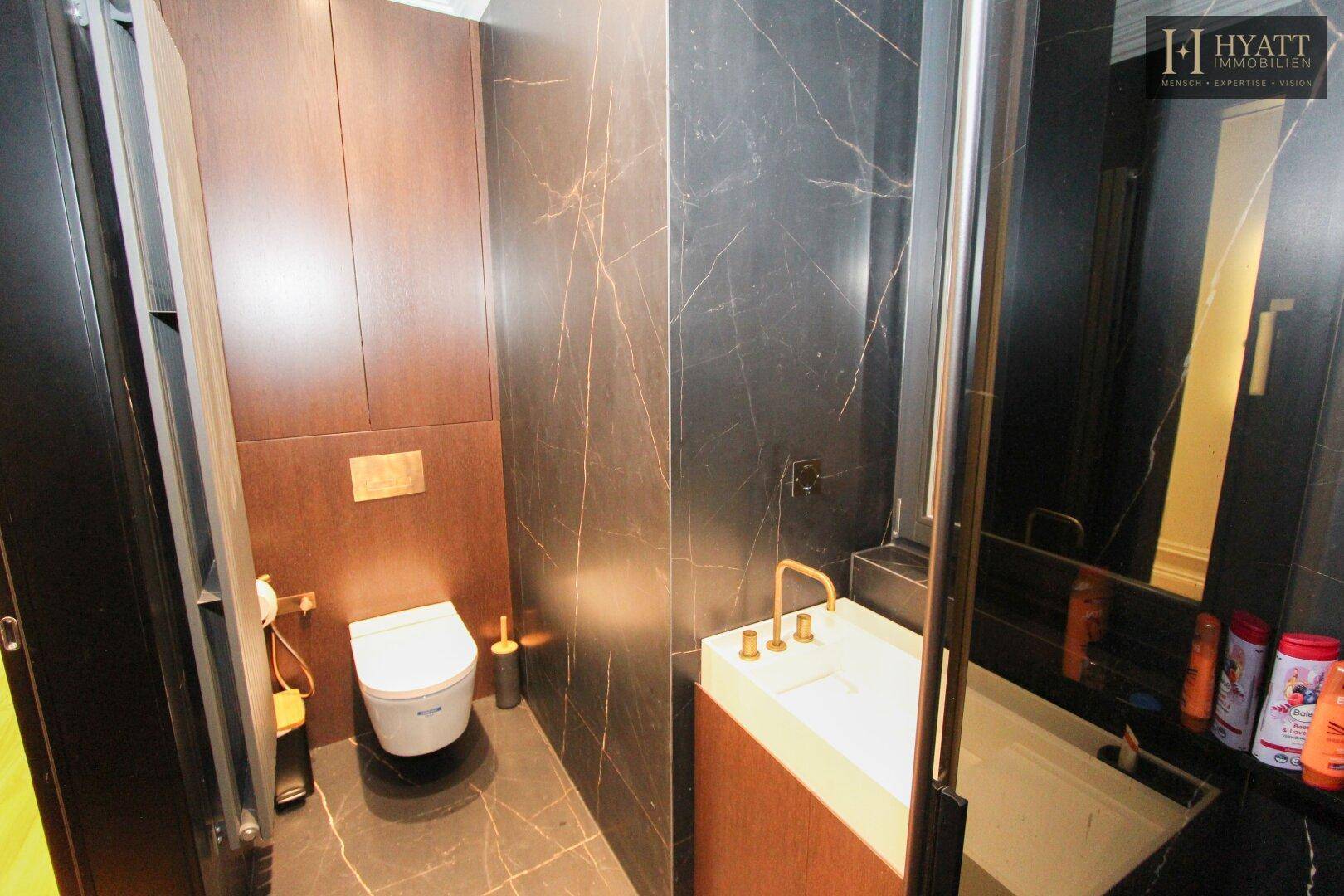 Modernes Gäste-WC mit dunklen Marmorfliesen, Holzverkleidung und Wand-WC.