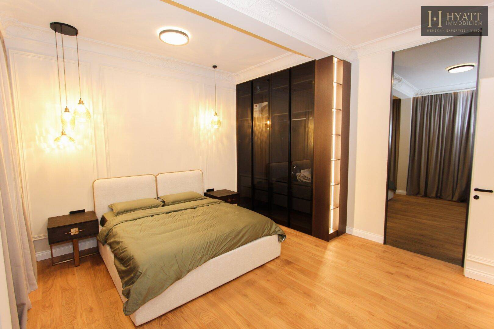 Elegantes Schlafzimmer mit Holzboden, dunklen Einbauschränken und dekorativen Leuchten.