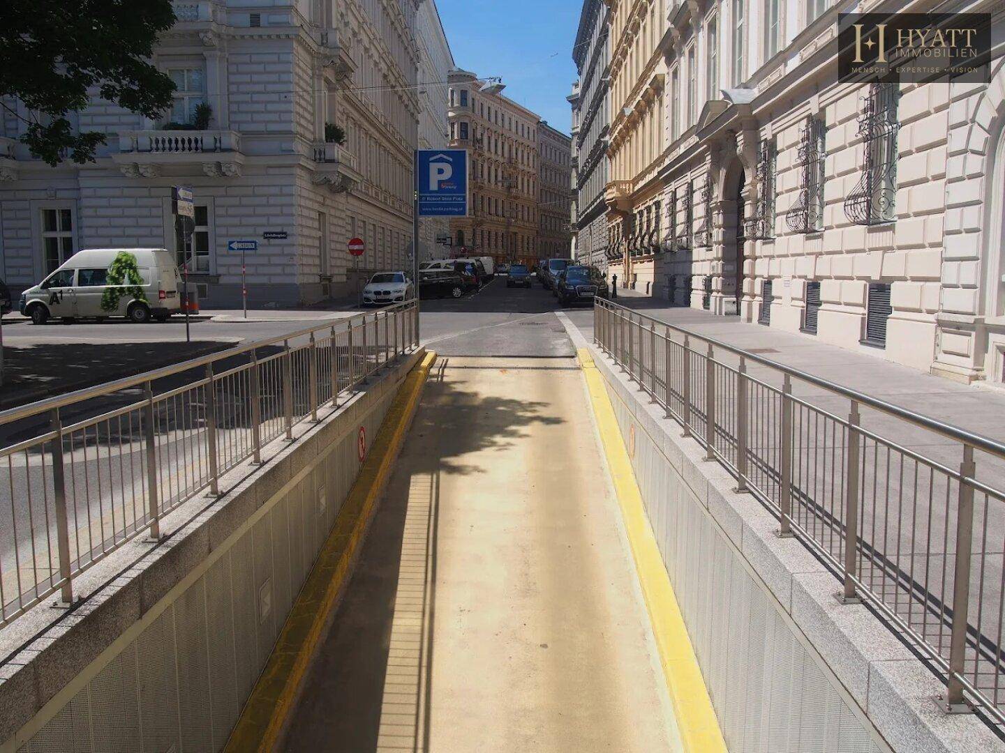 Einfahrt zur Tiefgarage von einer städtischen Straße mit umliegenden klassischen Gebäuden.