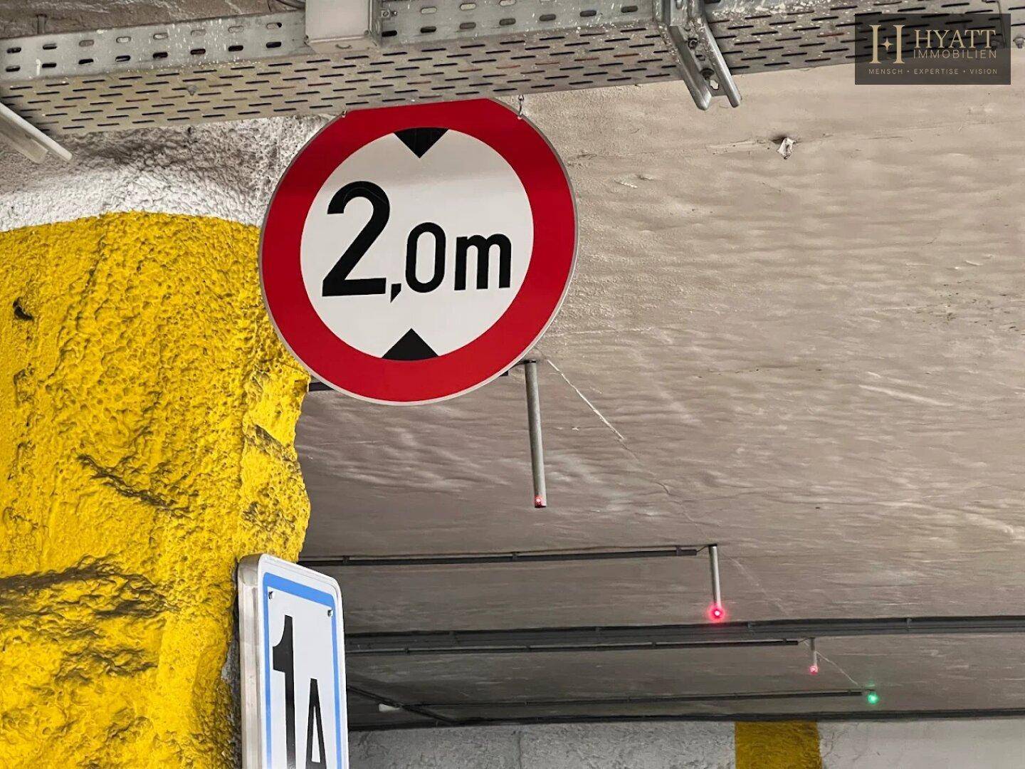 Nahaufnahme eines Höhenbegrenzungsschildes von 2,0m in einer Tiefgarage mit Betonwänden.