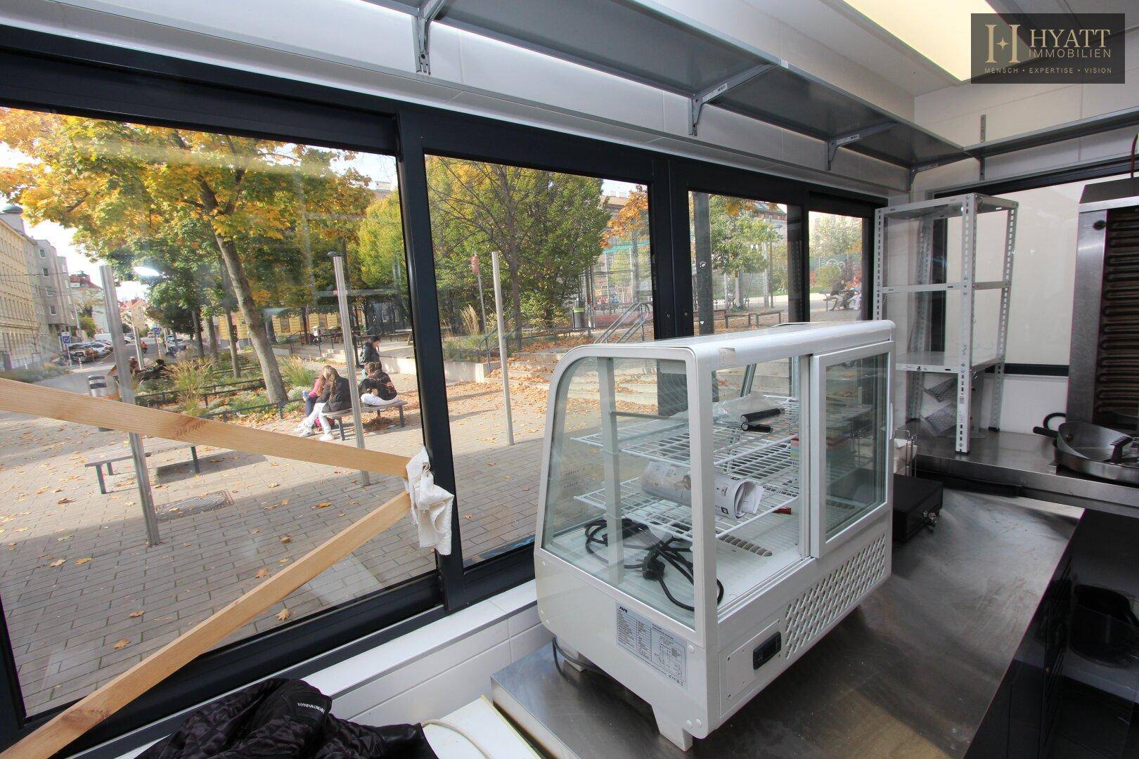 Innenansicht der Kiosk-Küche mit einer Kühlvitrine und großen Fenstern zum Außenbereich.