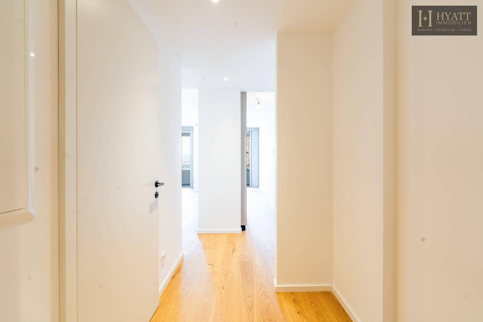 Heller Flur mit durchgehendem Holzfußboden, der die verschiedenen Bereiche der modernen Wohnung verbindet.