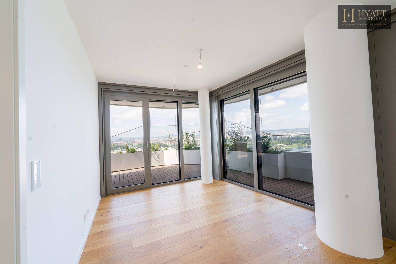 Heller Wohnbereich mit Holzboden und großen Schiebetüren, die auf einen Balkon führen.