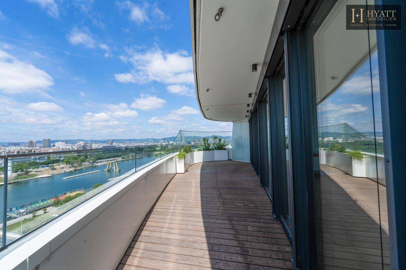 Langer Balkon mit Holzboden und Glasgeländer bietet einen weiten Blick auf die Stadt und den Fluss.