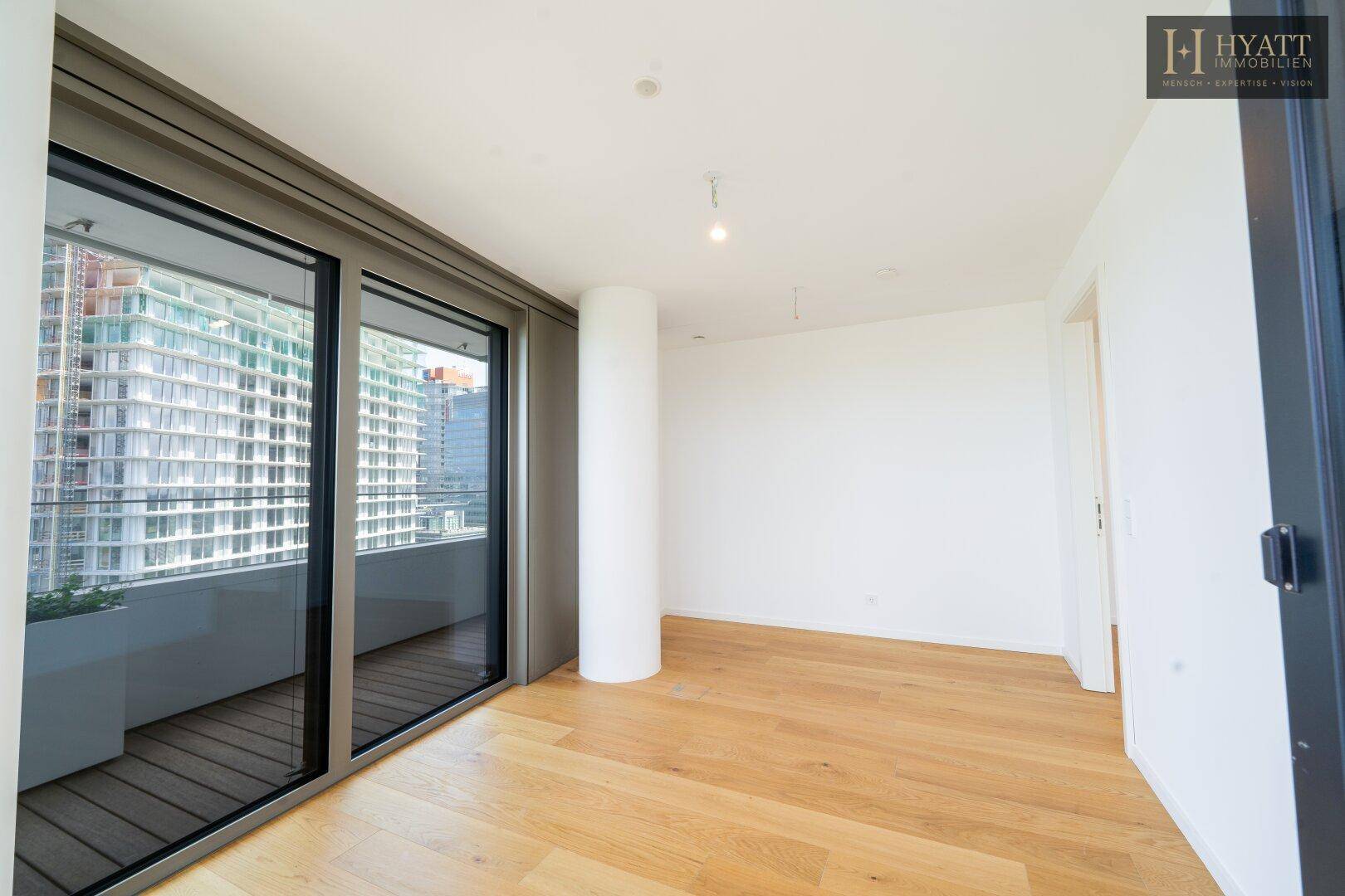 Helles Schlafzimmer mit Holzboden und Zugang zu einem Balkon mit Blick auf die Stadt.