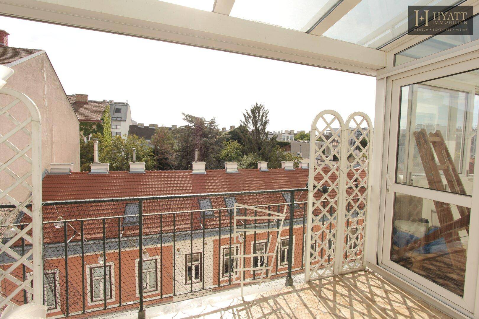 Verglaster Balkon mit Blick auf die umliegenden Dächer und Bäume in der Stadt.