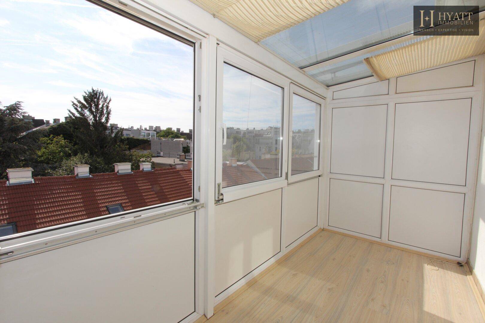 Heller, verglaster Balkon mit Holzfußboden und weitem Blick über die Stadtlandschaft.